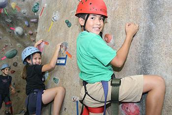 两个面带微笑的孩子穿着安全装备站在攀岩墙上
